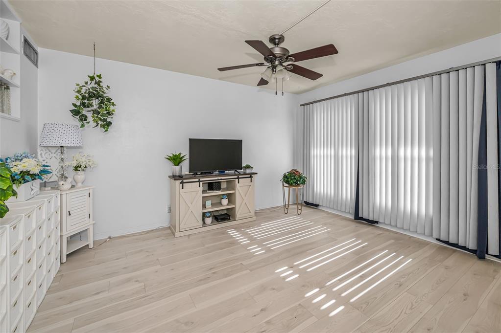 A living room with light wood-look flooring, a ceiling fan, and white vertical window blinds — 4051 58TH STREET N UNIT 243, KENNETH CITY, FL