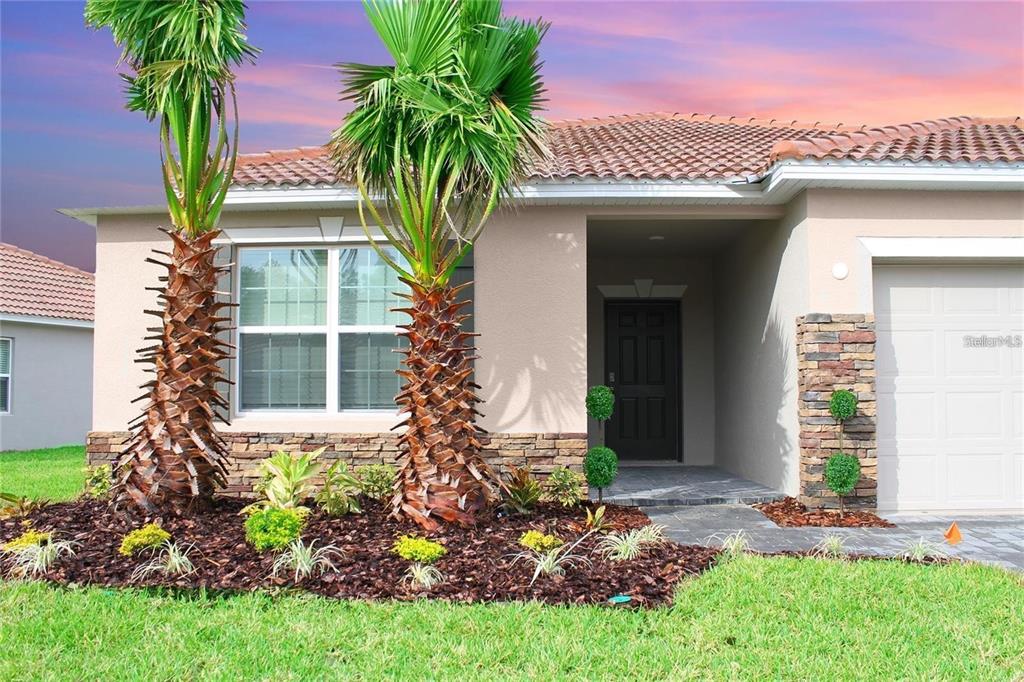 A single-story house exterior features a tiled roof, stone accents, and two palm trees — 1162 OAK BLUFF DRIVE, DAVENPORT, FL