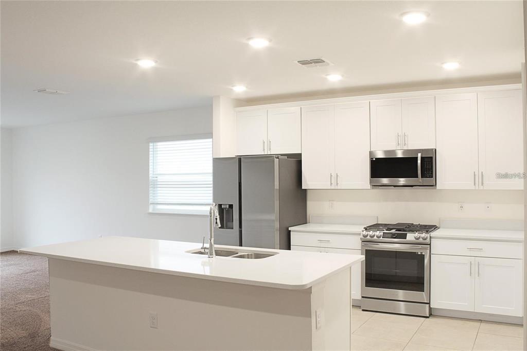 A modern kitchen features white cabinets, stainless steel appliances, and a central island with seating — 1162 OAK BLUFF DRIVE, DAVENPORT, FL