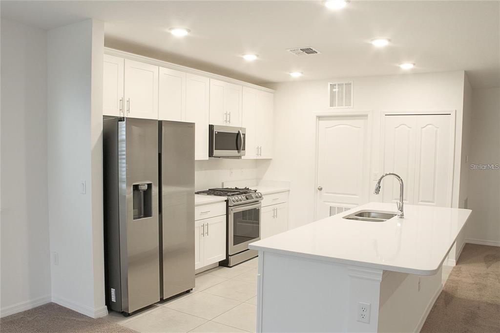 A modern kitchen features white cabinetry, stainless steel appliances, and a central island with sink — 1162 OAK BLUFF DRIVE, DAVENPORT, FL
