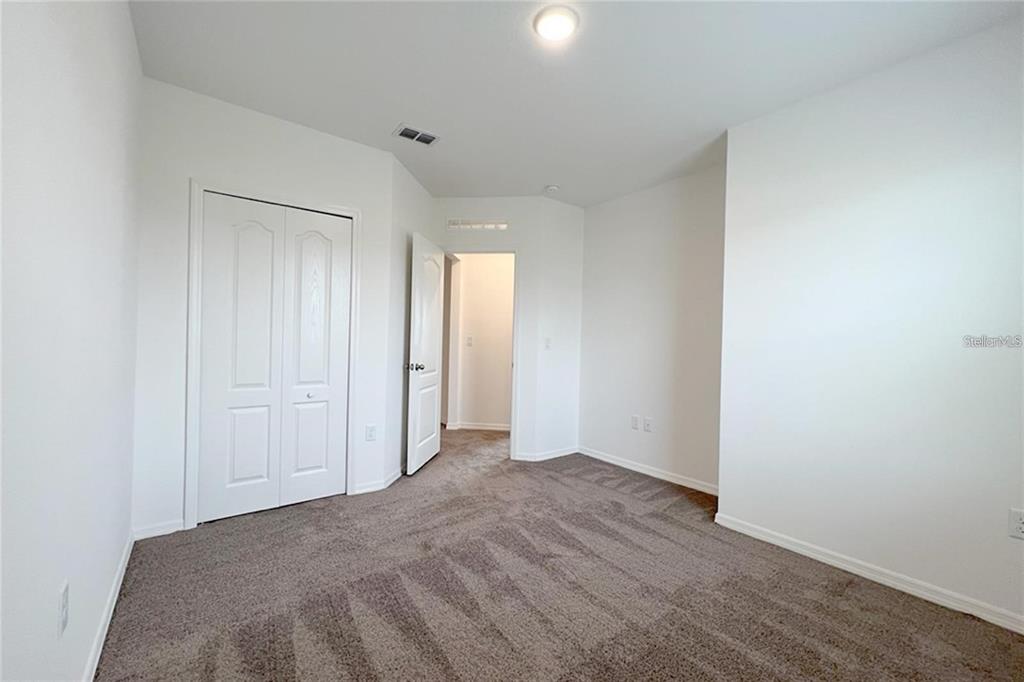An empty bedroom features white walls, beige carpeting, a closet, and an open doorway — 1162 OAK BLUFF DRIVE, DAVENPORT, FL