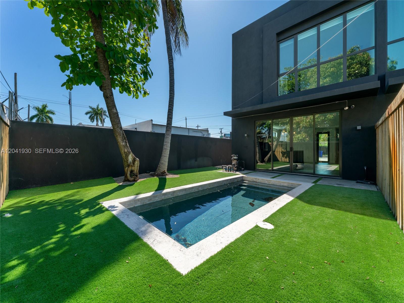 A modern black house features a small rectangular pool in a fenced artificial turf yard — 227 NW 39th St, Miami FL 33127, MIAMI, FL