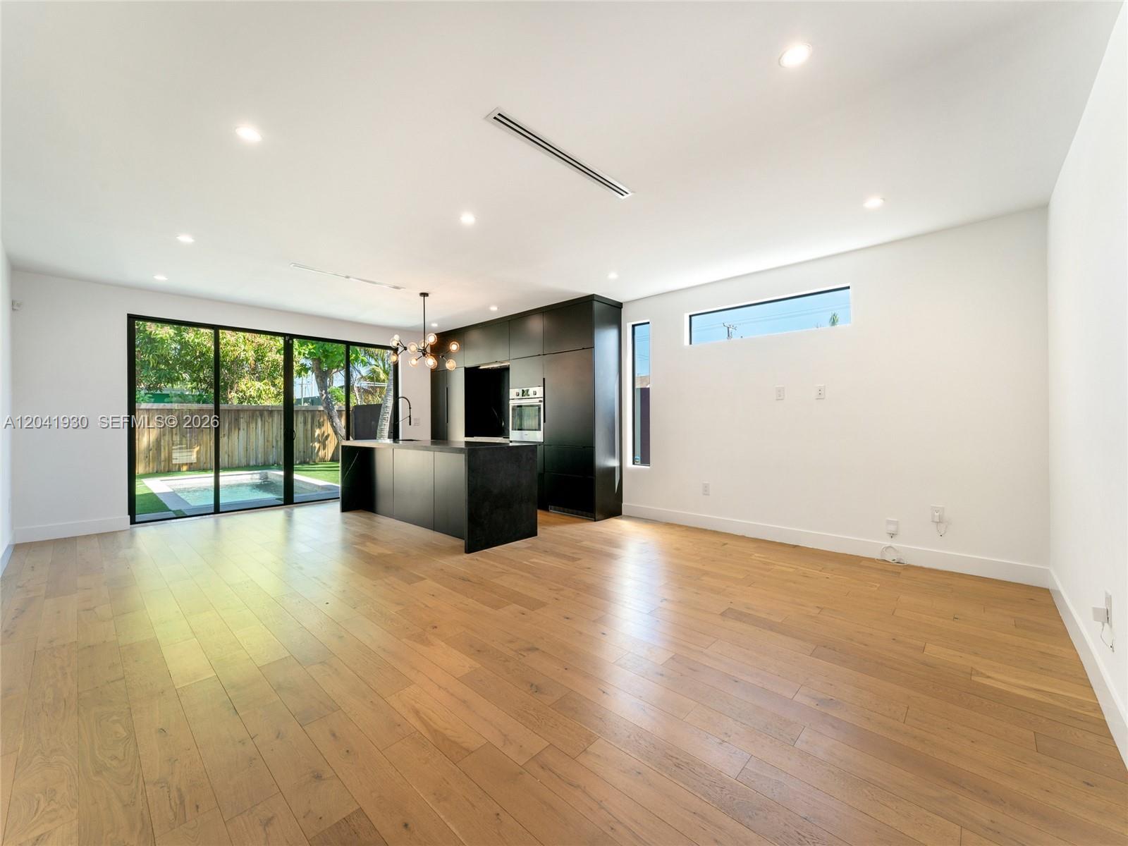 A modern kitchen with black cabinetry and a matching island overlooks a backyard pool — 227 NW 39th St, Miami FL 33127, MIAMI, FL