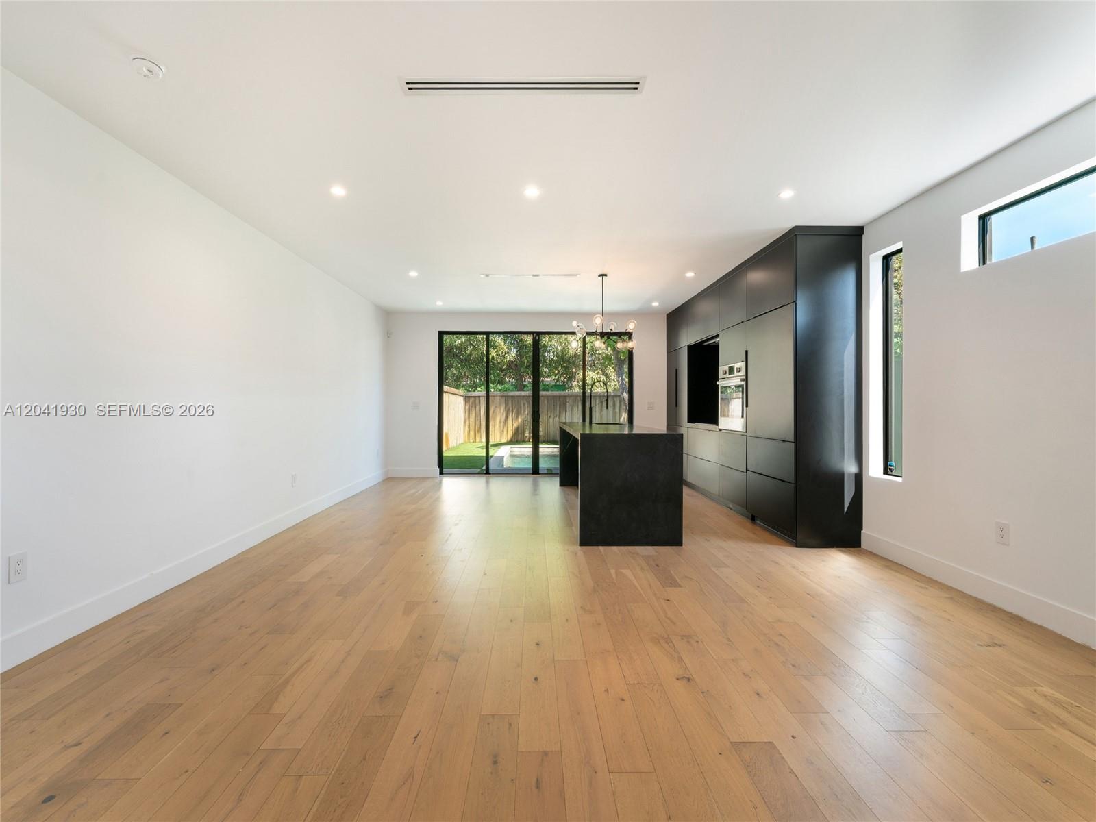A modern kitchen features black cabinetry, a central island, and light wood flooring — 227 NW 39th St, Miami FL 33127, MIAMI, FL