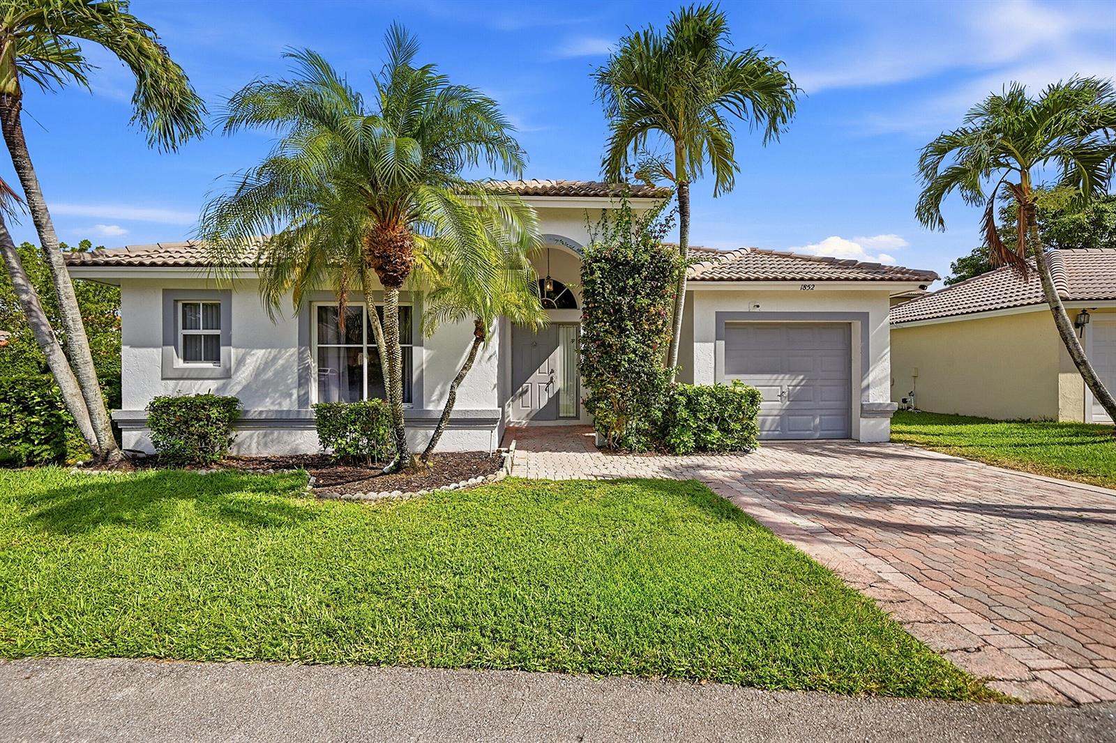 A single-story house with a paved driveway, palm trees, and a gray garage door — 1852 Capeside Circle, Wellington FL 33414, WELLINGTON, FL