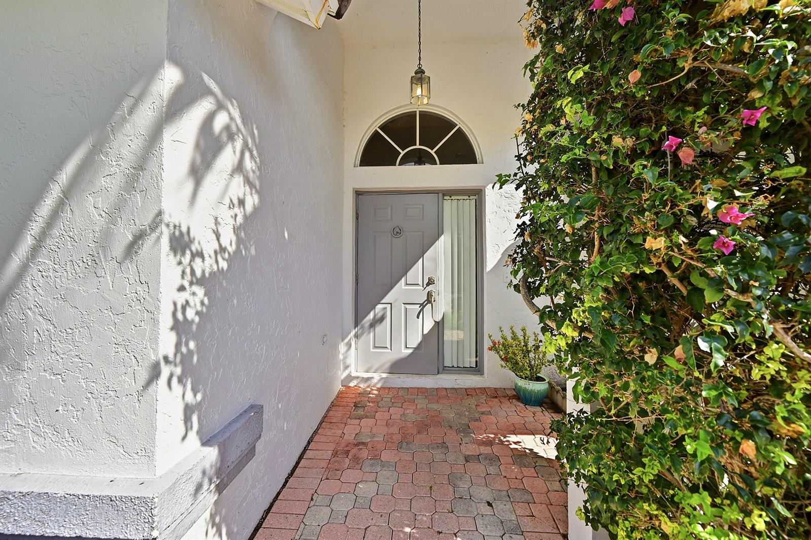 A gray front door with a sidelight and arched transom sits at the end of a brick walkway — 1852 Capeside Circle, Wellington FL 33414, WELLINGTON, FL