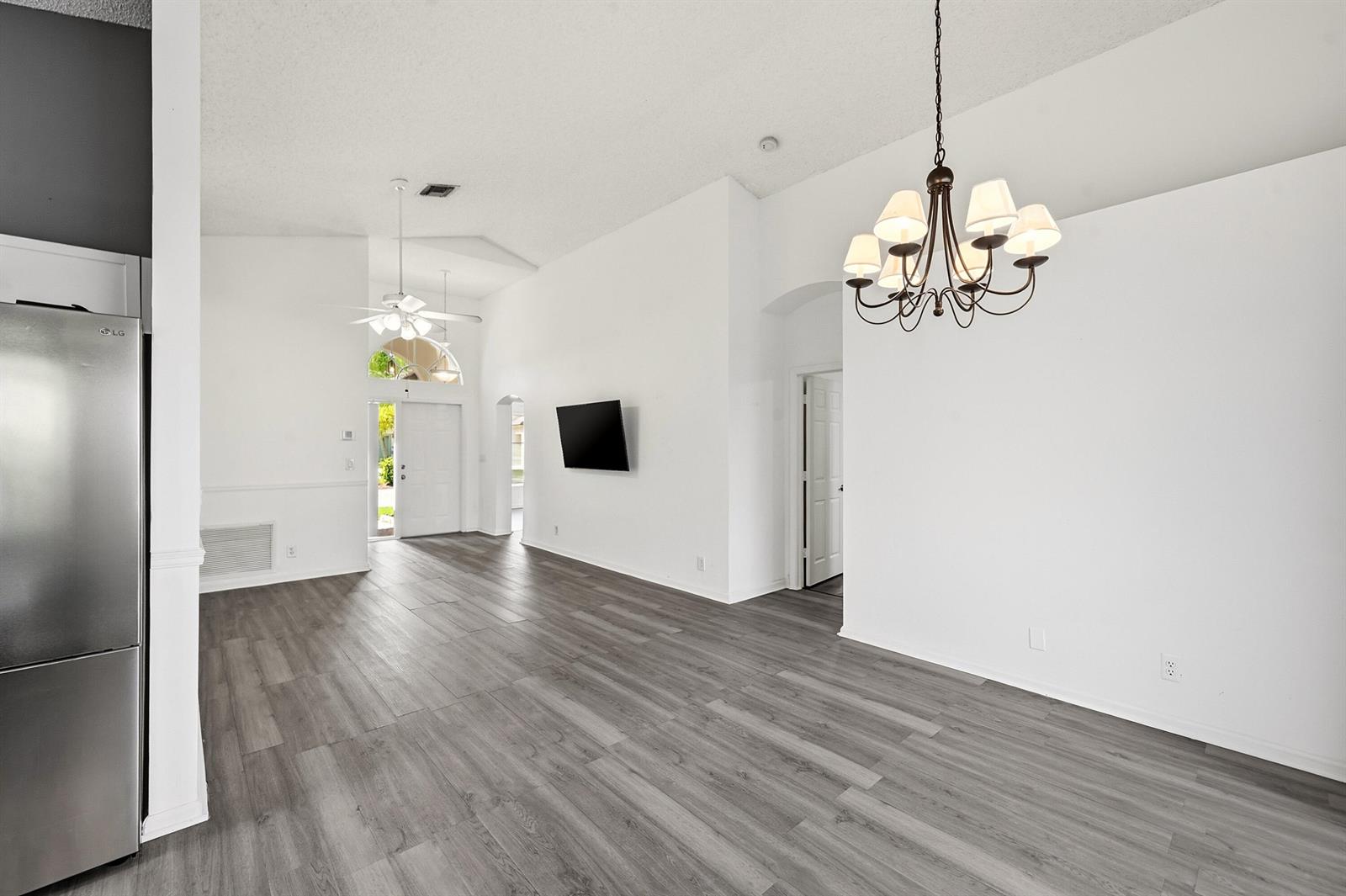 A bright, open-concept living area features white walls, gray wood-look flooring, and a chandelier — 1852 Capeside Circle, Wellington FL 33414, WELLINGTON, FL