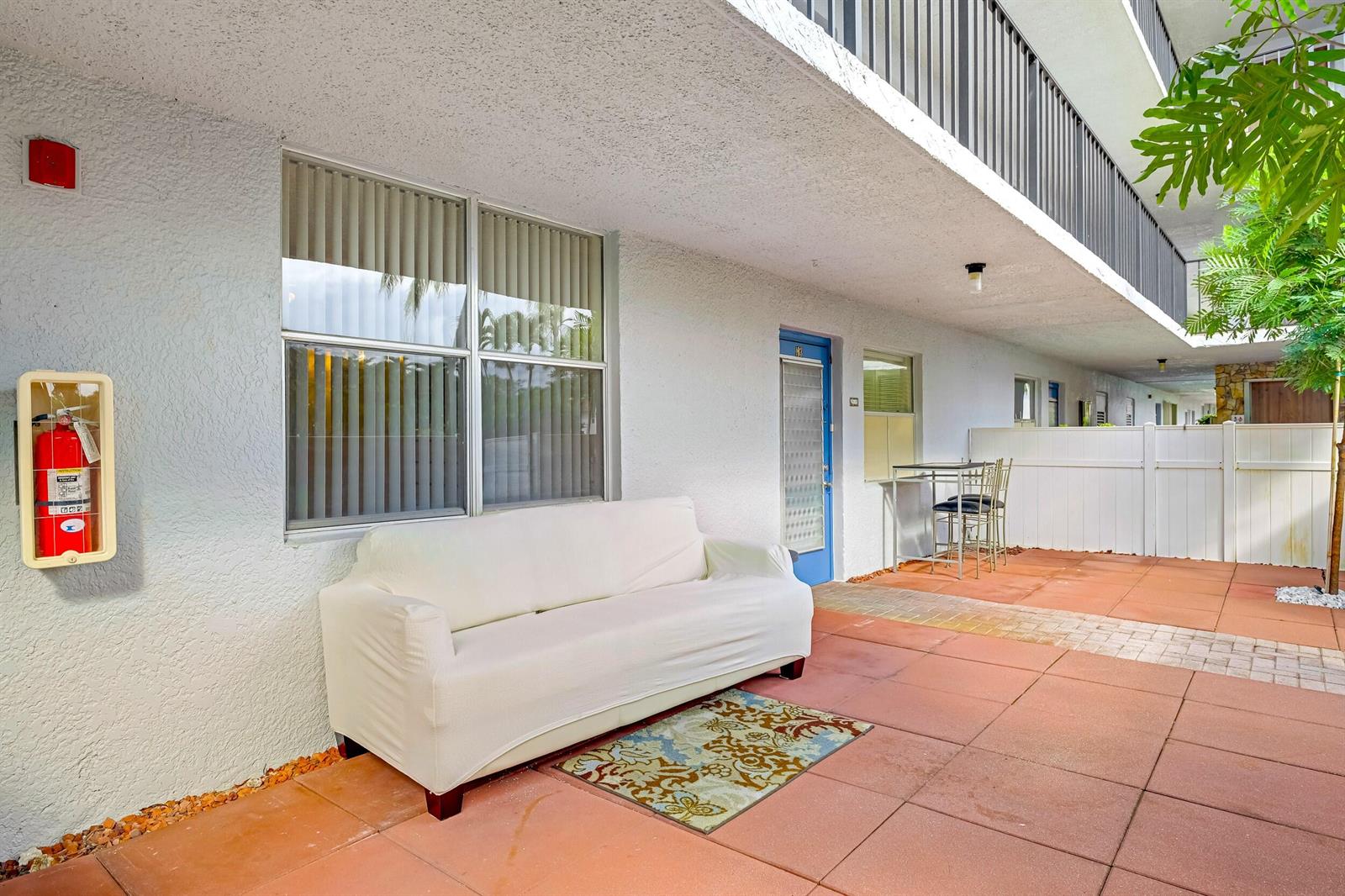 A white sofa sits on a tiled patio outside an apartment entrance with a fire extinguisher — 6650 S Oriole Boulevard # 1030, Delray Beach FL 33446, DELRAY BEACH, FL