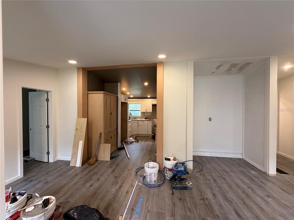 A room under renovation features wood-look flooring, a kitchen opening, and exposed wall patches — 11091 NE 107TH TERRACE, ARCHER, FL