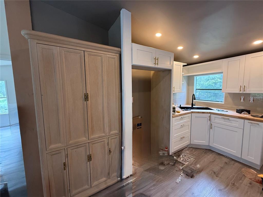 A kitchen features light wood cabinetry, white cabinets, a corner sink, and wood-look flooring — 11091 NE 107TH TERRACE, ARCHER, FL
