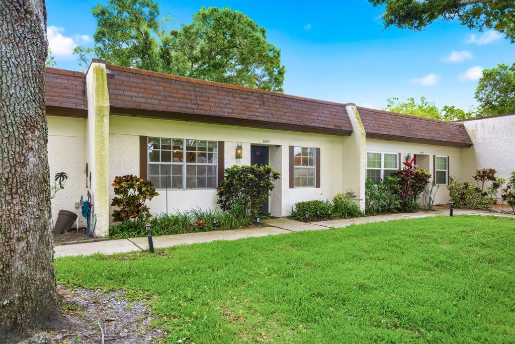 A single-story residential building with a brown shingled roof, white stucco walls, and front landscaping — 3127 MISSION GROVE DRIVE UNIT 3127, PALM HARBOR, FL