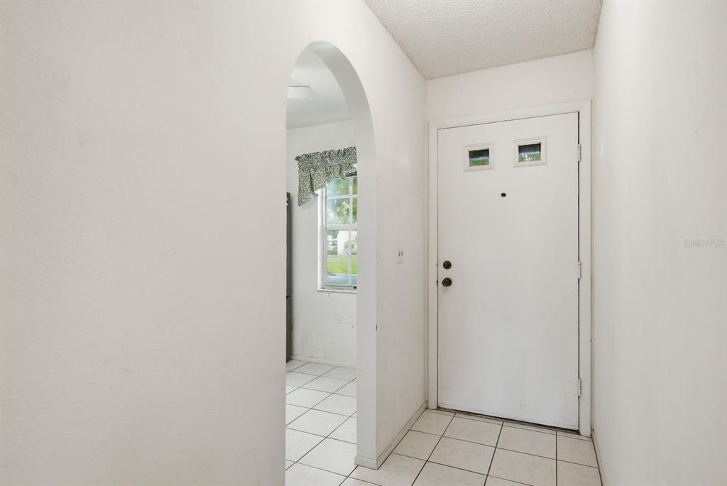 An entryway with white tile floors, a white door, and an arched doorway leading inside — 3127 MISSION GROVE DRIVE UNIT 3127, PALM HARBOR, FL