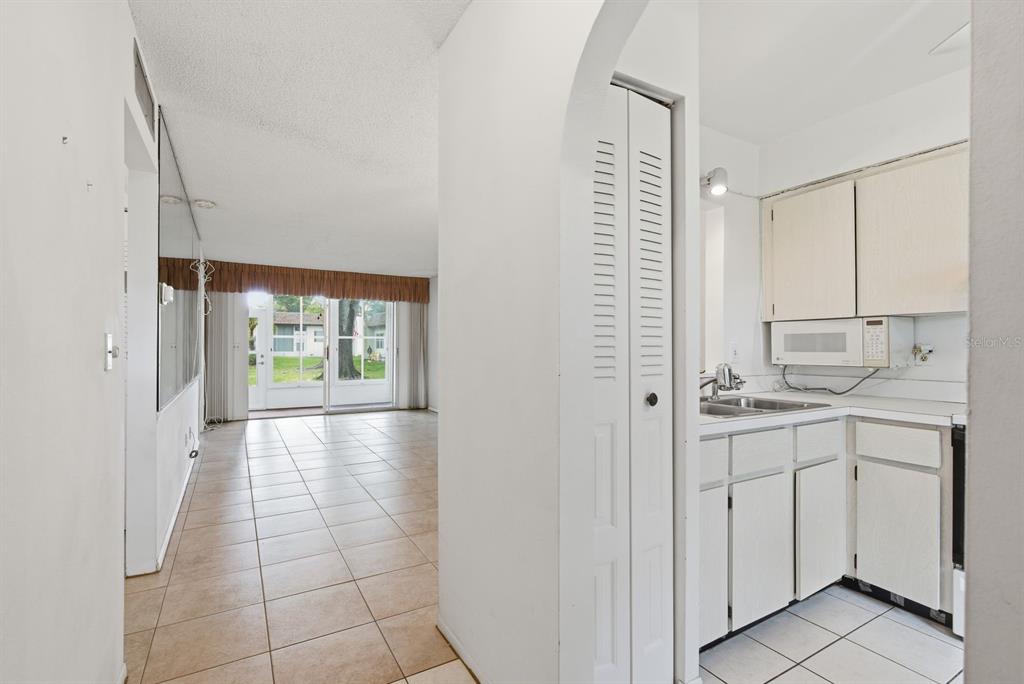 A view from a tiled kitchen looking toward a living area with sliding glass doors — 3127 MISSION GROVE DRIVE UNIT 3127, PALM HARBOR, FL