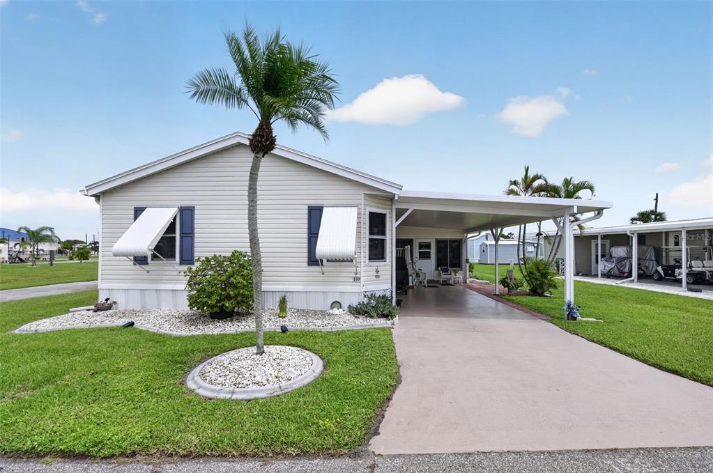 A single-story manufactured home with light siding, a palm tree, and an attached carport — 159 TARPON, PUNTA GORDA, FL