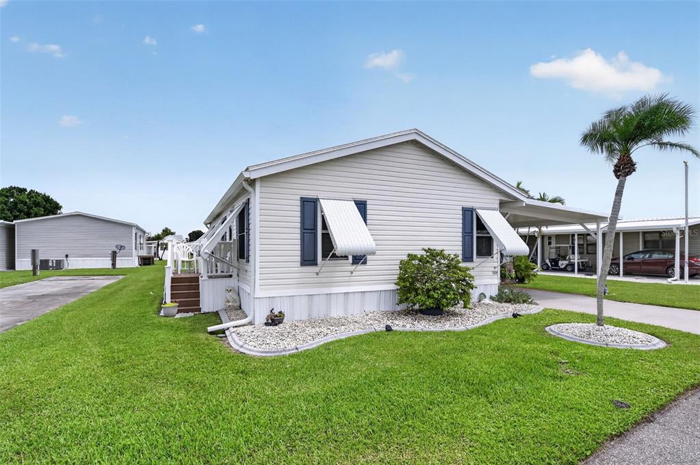 A light-colored manufactured home with a carport, white awnings, and a landscaped front yard — 159 TARPON, PUNTA GORDA, FL