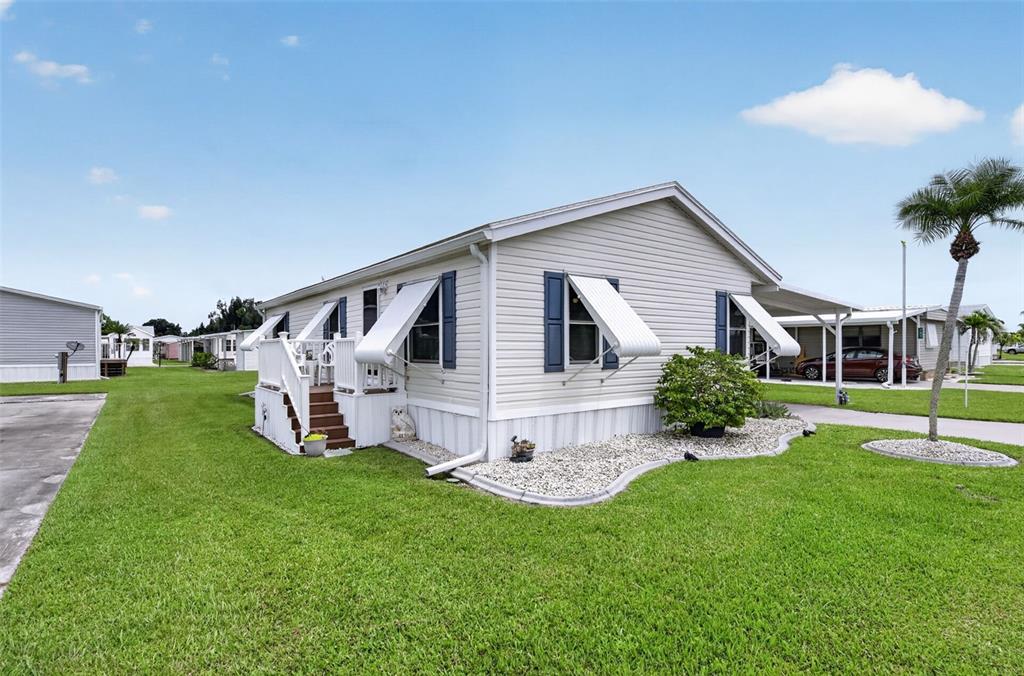 A single-story manufactured home with light siding, blue shutters, and a small wooden deck — 159 TARPON, PUNTA GORDA, FL