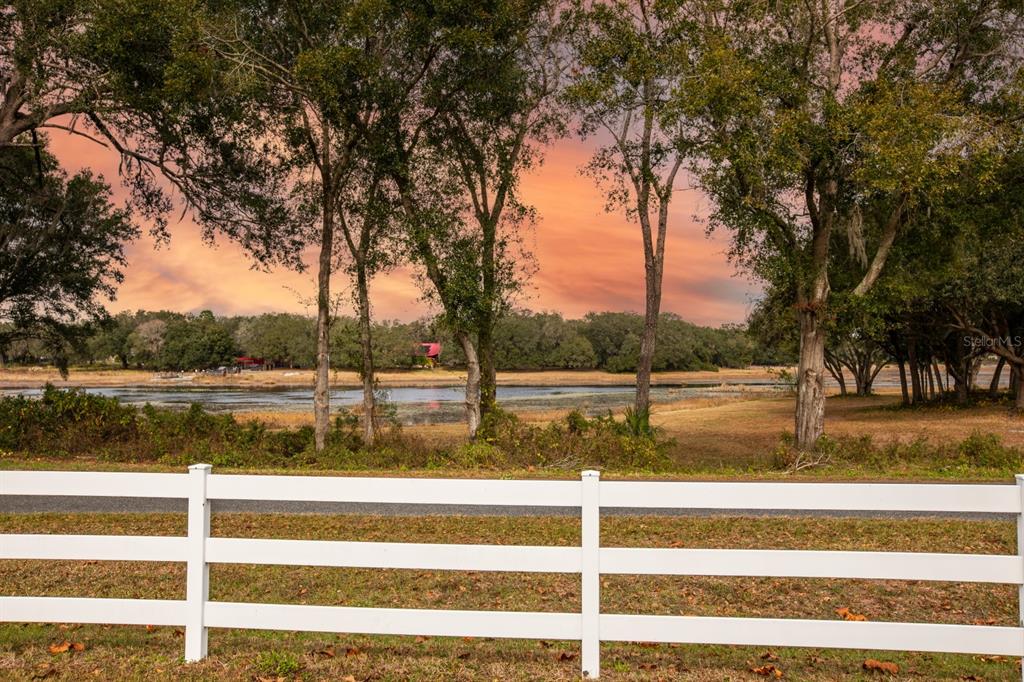 A white fence overlooks a grassy field, a pond, and trees under a sunset sky — 17520 SE 159TH TERRACE, WEIRSDALE, FL