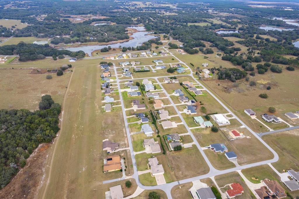 An aerial view shows a residential neighborhood with houses situated alongside a grass airstrip — 17520 SE 159TH TERRACE, WEIRSDALE, FL