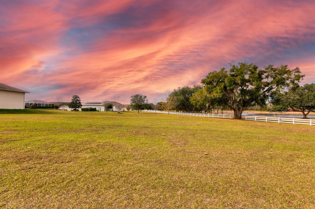 A large, grassy field with a white fence and trees under a vibrant sunset sky — 17520 SE 159TH TERRACE, WEIRSDALE, FL
