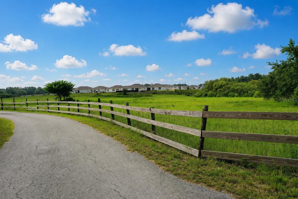 A paved path curves alongside a wooden fence bordering a grassy field with distant houses — 0 E HINSON AVENUE E, HAINES CITY, FL