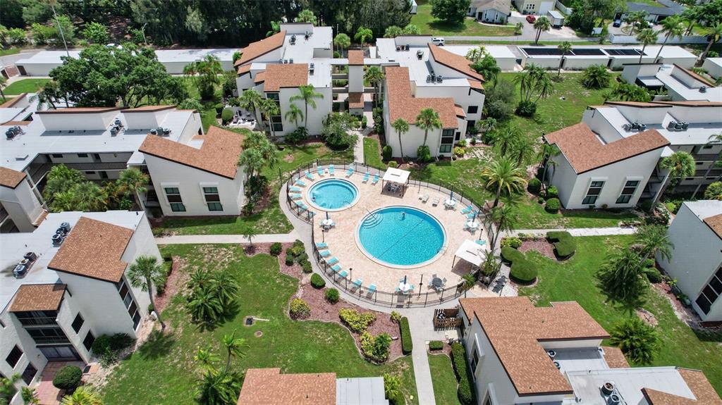An aerial view shows a residential complex with two connected swimming pools and surrounding buildings — 2207 BELLEAIR ROAD UNIT B16, CLEARWATER, FL