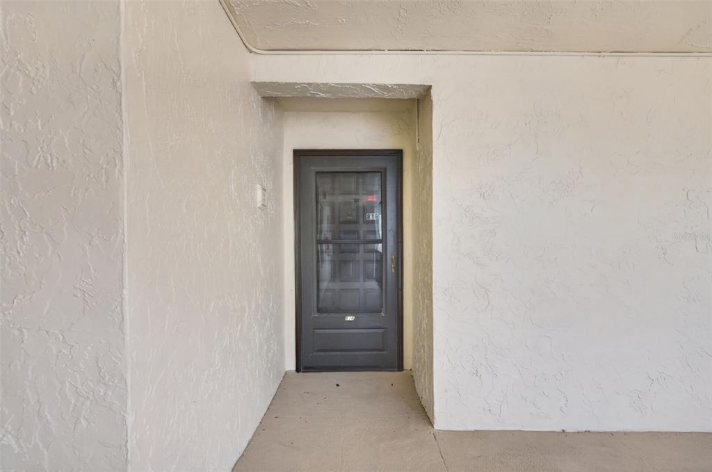 A dark gray storm door is set into a recessed entryway with textured white walls — 2207 BELLEAIR ROAD UNIT B16, CLEARWATER, FL