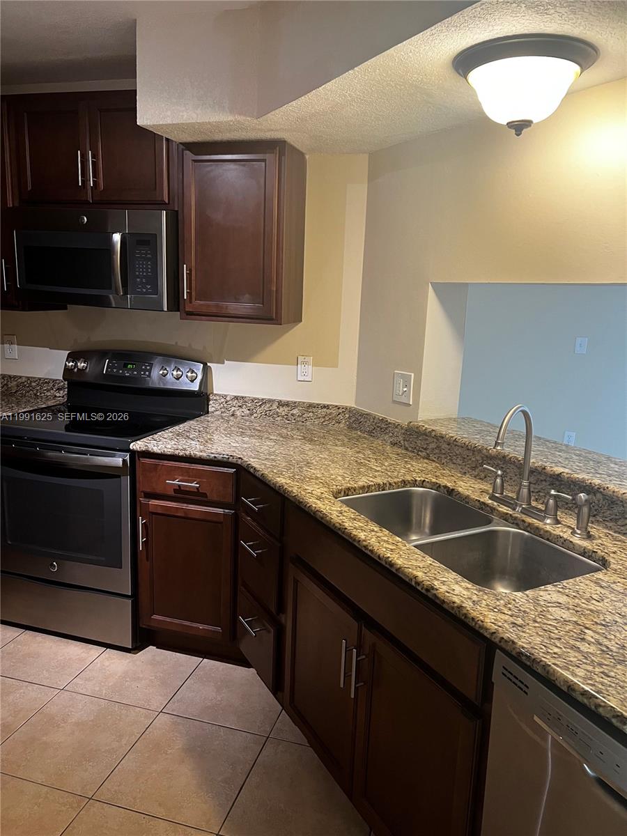 A kitchen features dark wood cabinets, granite countertops, stainless steel appliances, and tile flooring — 802 Constitution Dr # 802B, Homestead FL 33034, HOMESTEAD, FL