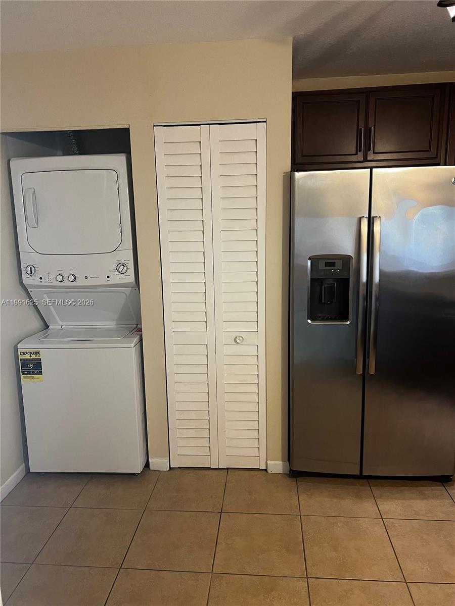 A laundry closet with a stacked washer-dryer unit sits next to a stainless steel refrigerator — 802 Constitution Dr # 802B, Homestead FL 33034, HOMESTEAD, FL