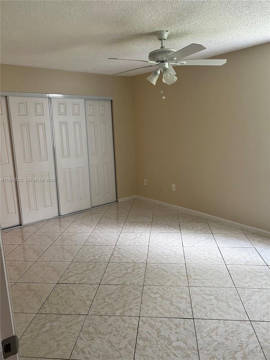 A bedroom with beige walls, white sliding closet doors, and light-colored tiled flooring — 802 Constitution Dr # 802B, Homestead FL 33034, HOMESTEAD, FL