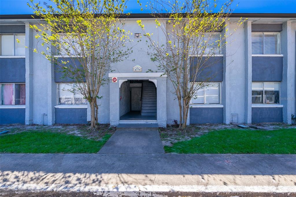 A two-story apartment building exterior features gray stucco walls, dark blue accents, and two trees — 4779 S TEXAS AVENUE UNIT 4779D, ORLANDO, FL