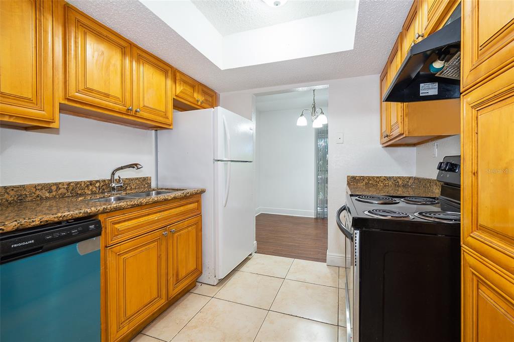 A galley kitchen features honey-oak cabinets, granite countertops, black appliances, and light-colored floor tiles — 4779 S TEXAS AVENUE UNIT 4779D, ORLANDO, FL