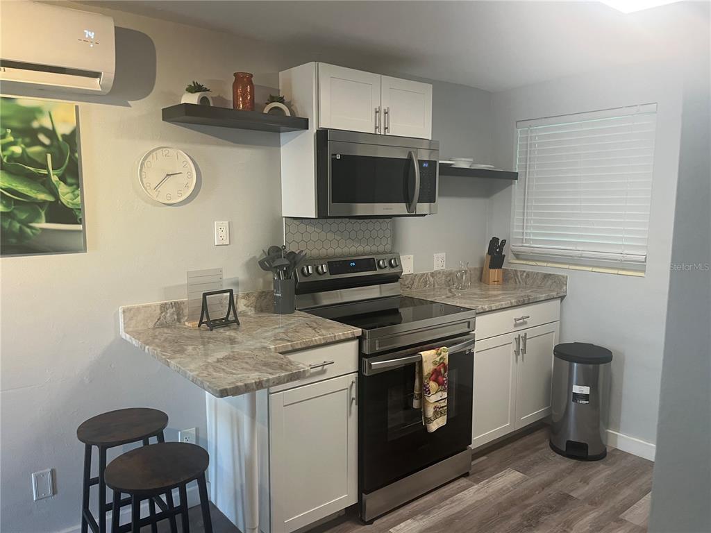 A kitchen features white cabinets, stainless steel appliances, a patterned countertop, and a small breakfast bar — 115 CLEVELAND AVENUE, LARGO, FL