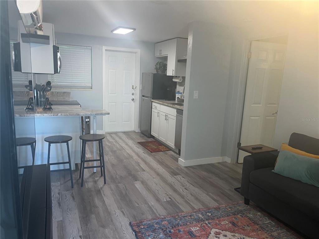 A small kitchen with white cabinets and a breakfast bar opens into a living area — 115 CLEVELAND AVENUE, LARGO, FL