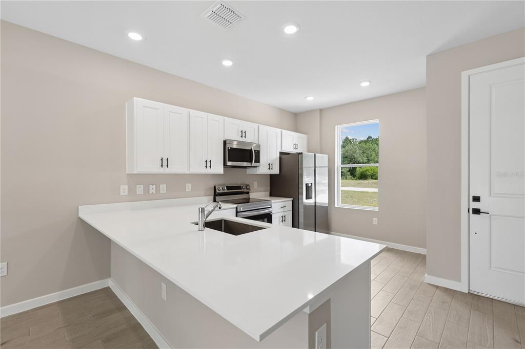 A modern kitchen features white cabinets, stainless steel appliances, and a large white quartz island — 2910 SW 165 STREET ROAD, OCALA, FL