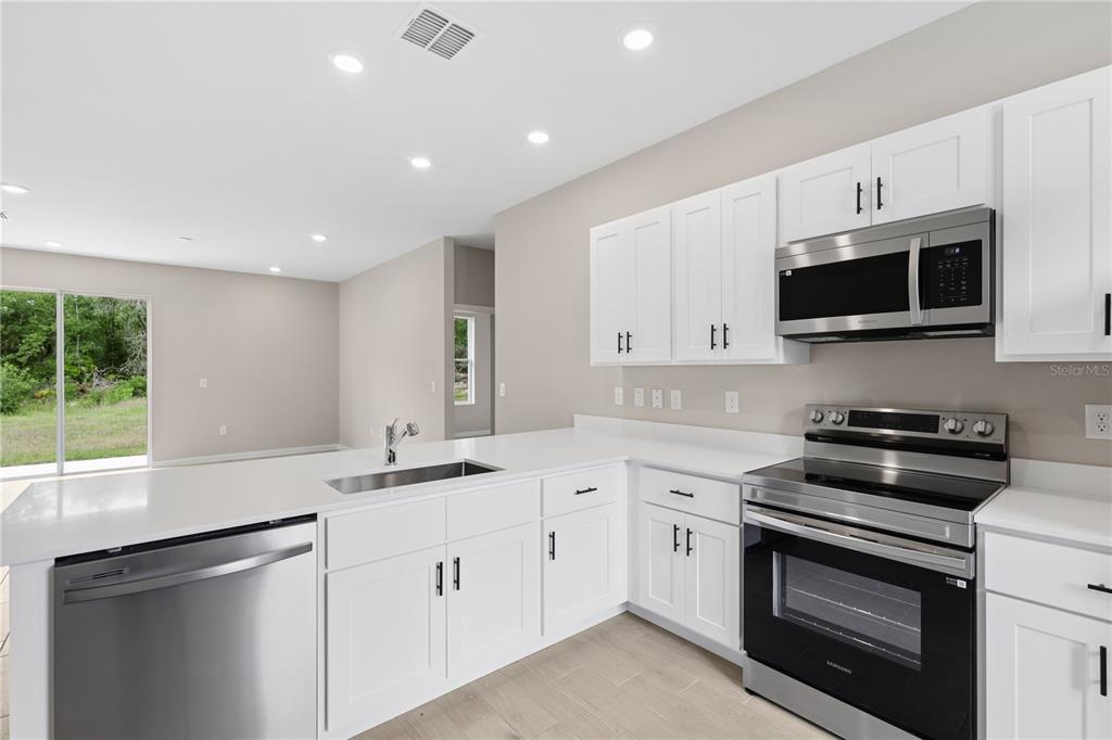 A modern kitchen features white cabinets, stainless steel appliances, and white countertops — 2910 SW 165 STREET ROAD, OCALA, FL