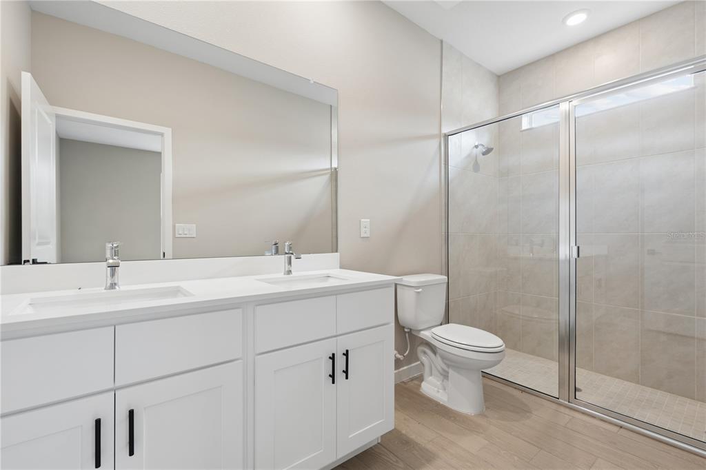 A bathroom features a double vanity with white cabinets, a mirror, and a glass-enclosed shower — 2910 SW 165 STREET ROAD, OCALA, FL