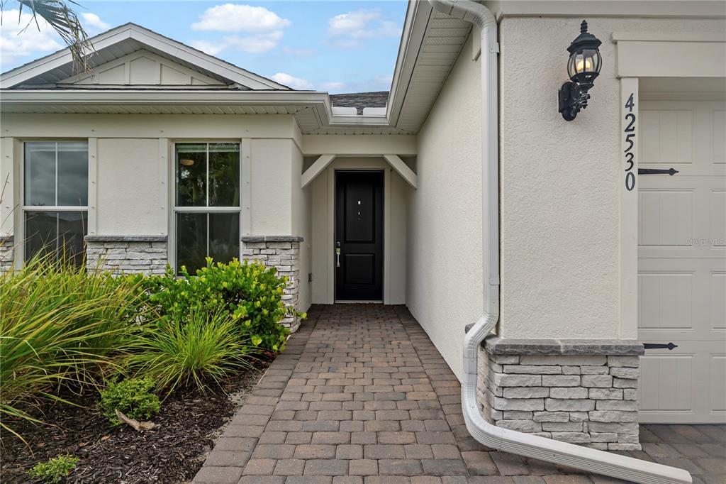 A paved walkway leads to the black front door of a house with stone accents — 42530 ATLAS DRIVE, PUNTA GORDA, FL