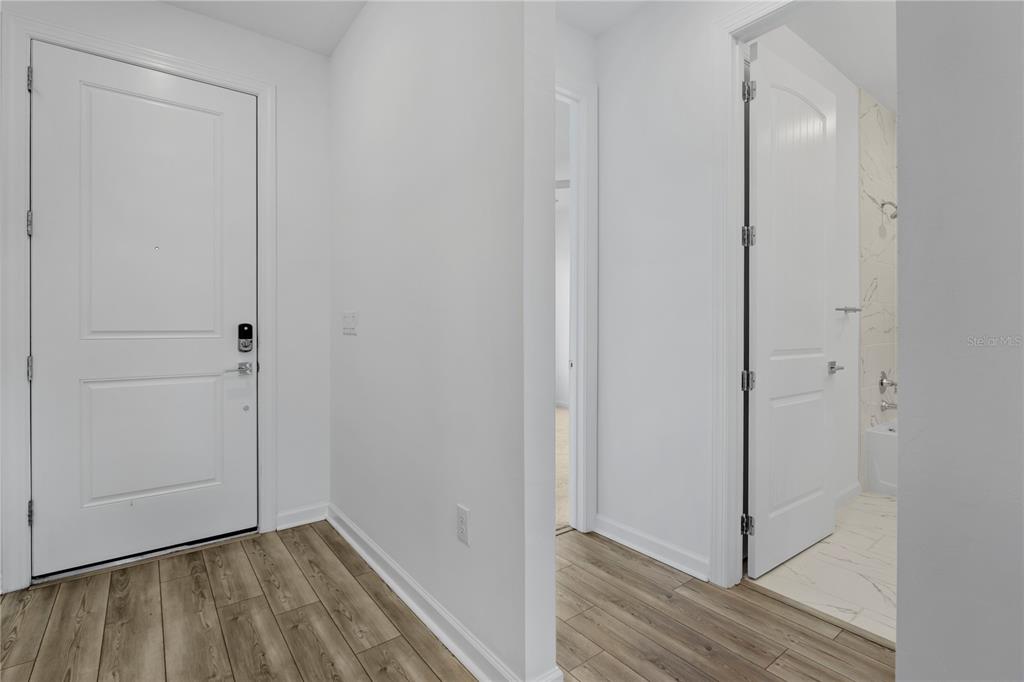 A hallway with wood-look flooring leads to a bathroom with marble-style tile and a door — 42530 ATLAS DRIVE, PUNTA GORDA, FL