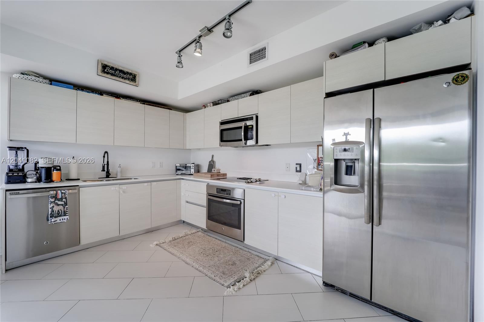 A modern kitchen features light wood cabinets, stainless steel appliances, and white tiled flooring — 4250 Biscayne Blvd # 301, Miami FL 33137, MIAMI, FL