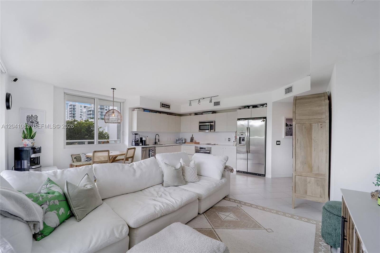 A bright open-concept living room and kitchen feature white cabinetry, stainless appliances, and tile flooring — 4250 Biscayne Blvd # 301, Miami FL 33137, MIAMI, FL