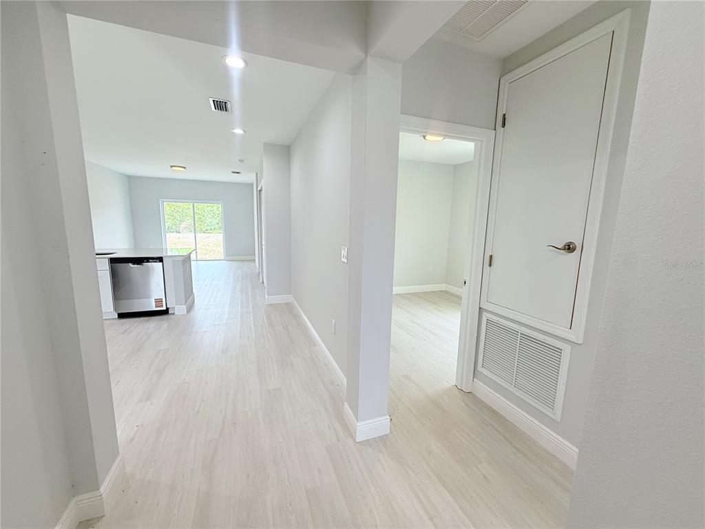 A hallway with light wood-look flooring leads to a kitchen and an adjacent bedroom — 11225 PENDLETON AVENUE, ENGLEWOOD, FL