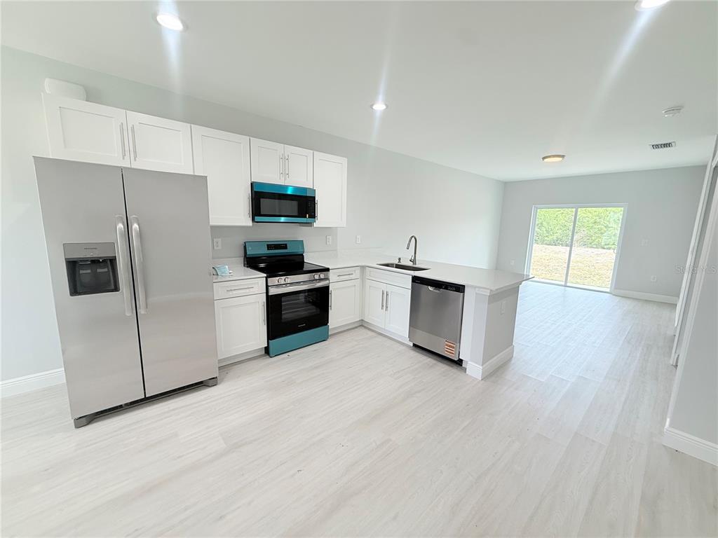 A modern kitchen features white cabinets, stainless steel appliances, and light wood-look flooring — 11225 PENDLETON AVENUE, ENGLEWOOD, FL