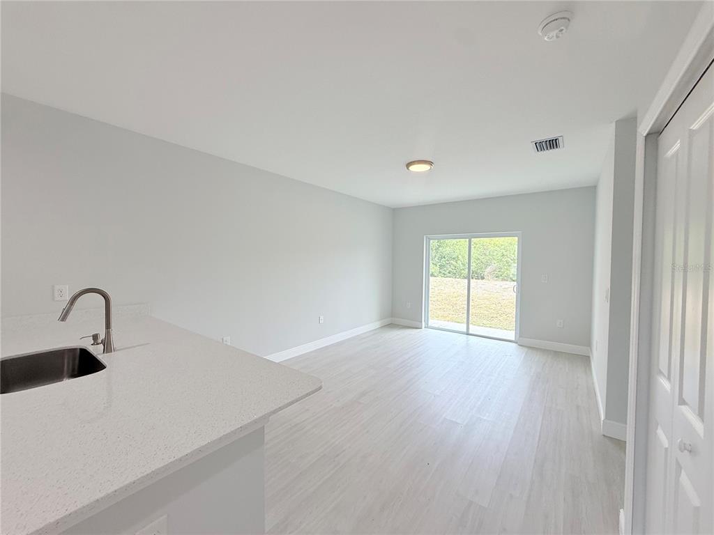 A kitchen counter with a sink overlooks an empty room with light flooring and sliding doors — 11225 PENDLETON AVENUE, ENGLEWOOD, FL