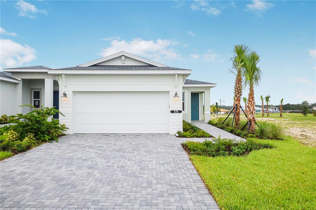 The exterior of a single-story house features a white garage, a paved driveway, and landscaping — 570 HAMMOCK OAKS BOULEVARD, LADY LAKE, FL