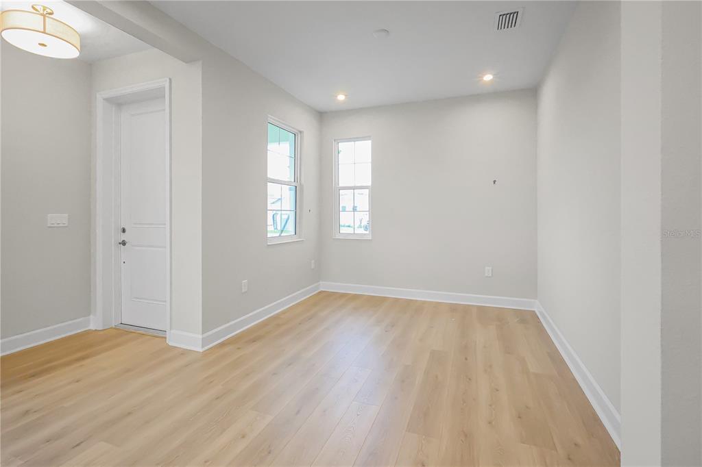 An empty room with light wood flooring, white walls, two windows, and a white door — 570 HAMMOCK OAKS BOULEVARD, LADY LAKE, FL