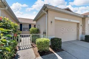 A beige house exterior features a garage, a small gated courtyard, and manicured landscaping — 1032 RADISON AVENUE UNIT 2, SUN CITY CENTER, FL