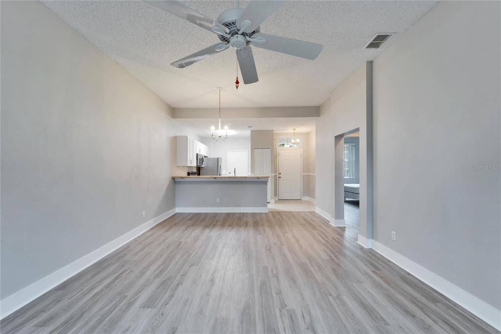 A living room with light wood-look flooring, a ceiling fan, and an open kitchen beyond — 1032 RADISON AVENUE UNIT 2, SUN CITY CENTER, FL