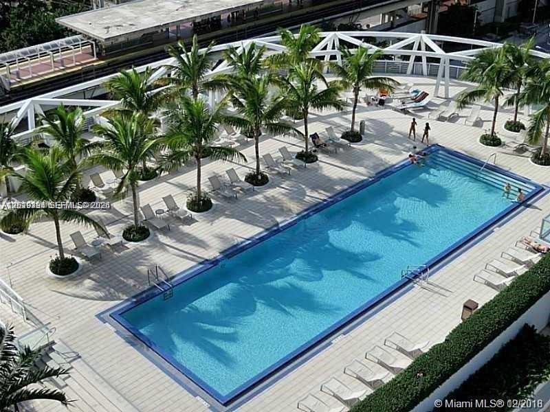 An aerial view shows a rectangular swimming pool surrounded by lounge chairs and palm trees — 1111 SW 1 ave # 2215, Miami FL 33130, MIAMI, FL