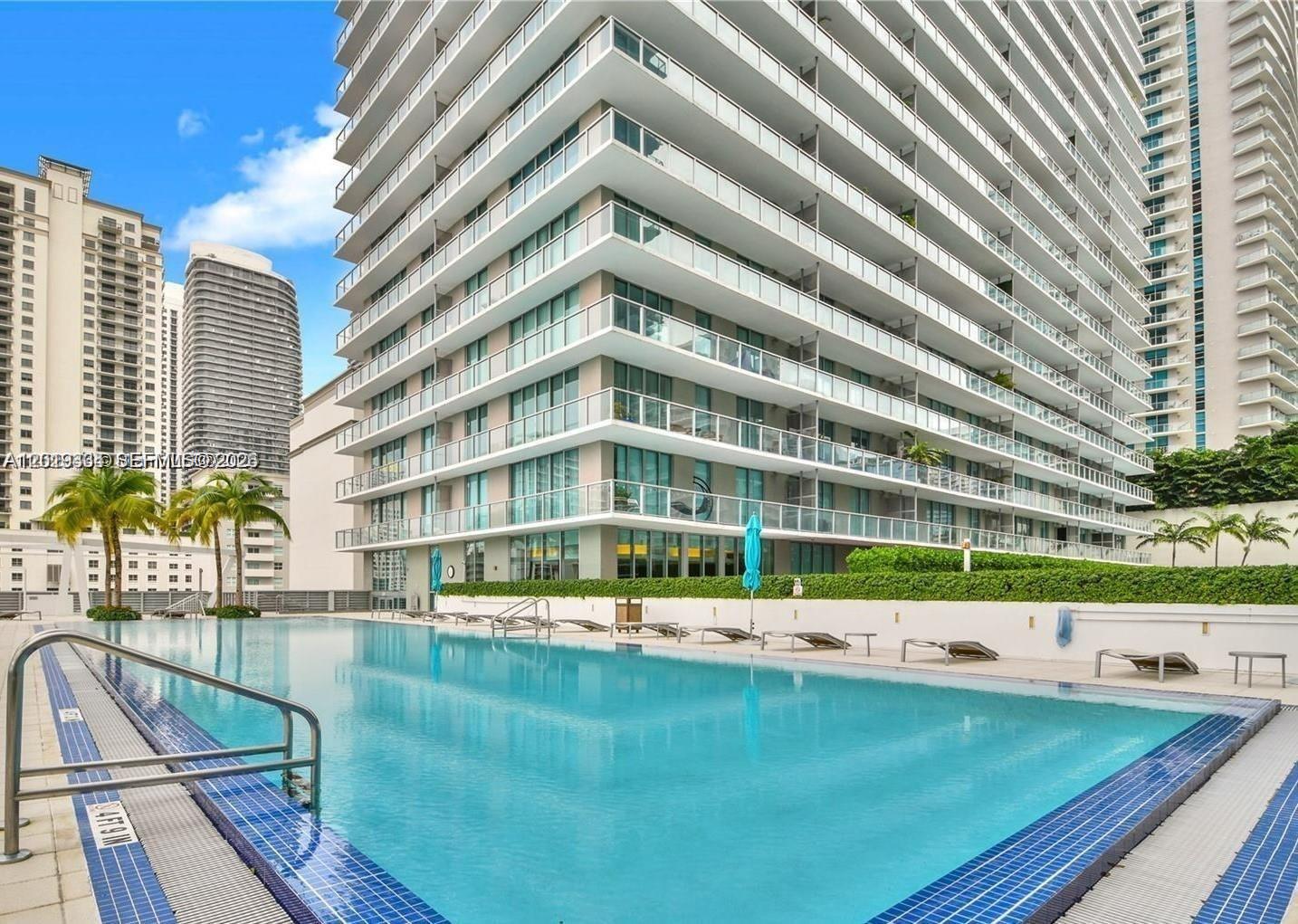 A swimming pool sits on a terrace in front of a modern high-rise apartment building — 1111 SW 1 ave # 2215, Miami FL 33130, MIAMI, FL