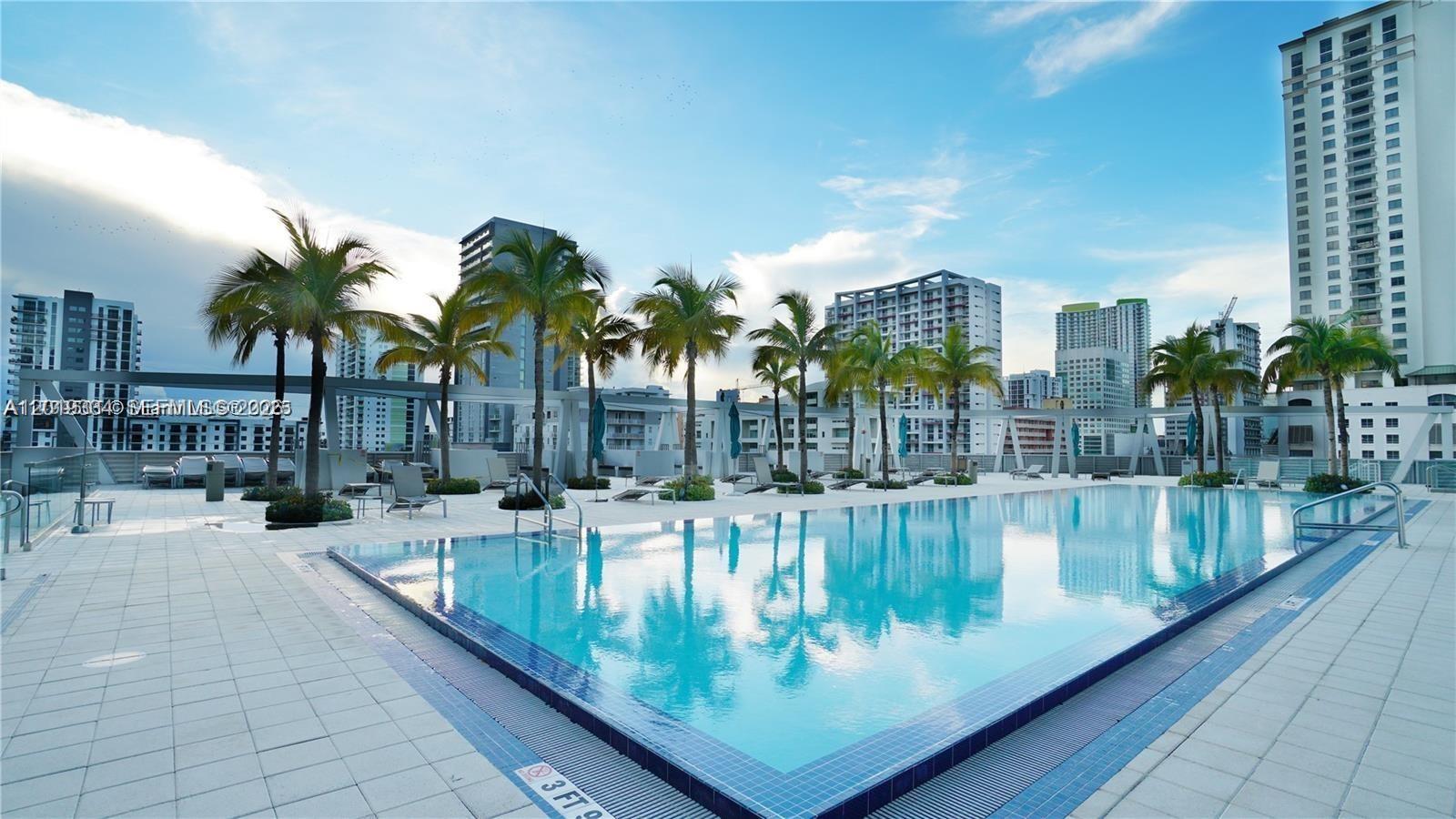 A rooftop swimming pool surrounded by palm trees and high-rise buildings under a blue sky — 1111 SW 1 ave # 2215, Miami FL 33130, MIAMI, FL